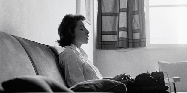 schwarz-weiß-Foto einer Frau, die mit einer Schreibmaschine auf dem Schoß auf einem Sofa sitzt