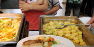 Ein Löffel schaufelt Kartoffeln auf einen Teller mit Fisch und Gemüse
