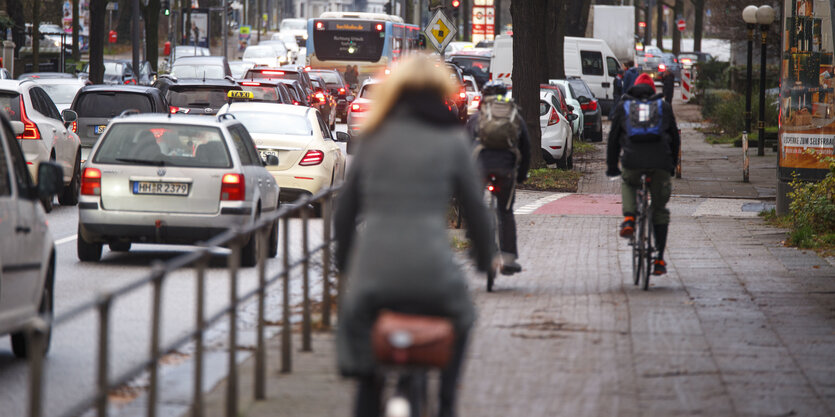 Eine Frau auf einem gepflasterten Radweg, links ein Geländer und Autos, rechts Fußgäünger