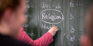 Ein Schüler schreibt das Wort Religion auf eine Schultafel