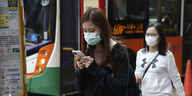 Eine Passantin mit Mundschutz blickt auf ihr Handy.