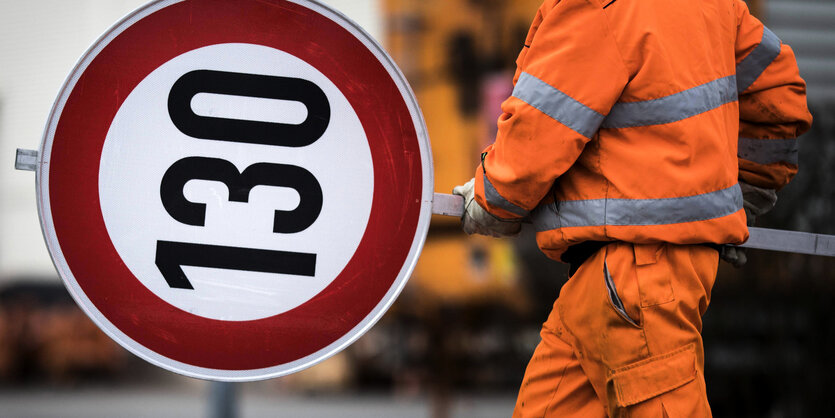 Ein Mitarbeiter einer Autobahnmeisterei trägt ein Schild mit dem Tempolimit 130.