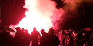 vermummte Demonstranten zünden im Dunkeln Pyrotechnik