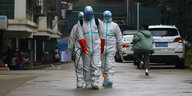 Drei Menschen in Schutzanzügen versprühen ein Desinfektionsmittel auf einer Straße