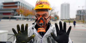 Ein Klimaaktivist hält seine schwarz verschmierten Hände hoch.
