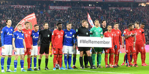 Fußballer von Schalke und Bayern stehen nebeneinander, einer hält ein Schild, auf dem steht „#WeRemember“