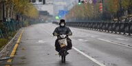 Ein Mopedfahrer mit Mundschutz auf einer ansonsten leeren Straße