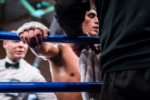 Ein Boxer hält sich am Ringseil fest, während er betreut wird Ein Boxer hält sich am Ringseil fest, während er betreut wird