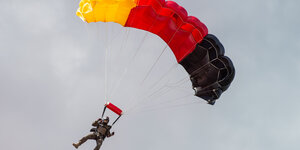Ein Springer hängt an einem Fallschirm aus gelben, rotem und schwarzem Stoff