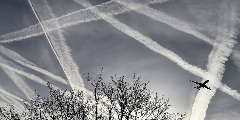 Ein Flugzeug am Himmel zwischen Kondensstreifen.