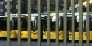 Nahverkehrsbusse stehen geparkt hinter einem Tor.