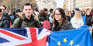 Eine Studentin und ein Student halten die Eu-Fahne und die britische Fahne und posieren für die Kamera