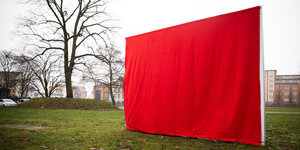 Auf einer Wiese steht ein mit einem roten Tuch verhülltest Wahlplakat der Hamburger Linken