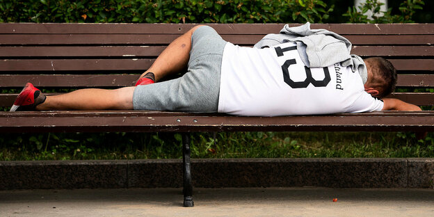 Ein Mann liegt auf einer Parkbank und schläft