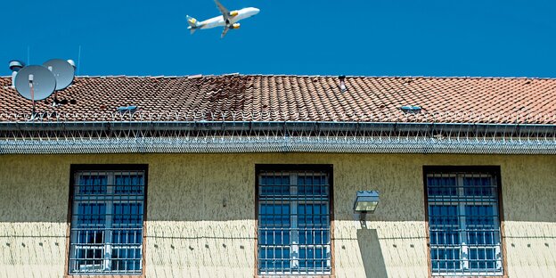 Abschiebungsgefängnis Langenhagen: Ein gelber Bau mit Gittern vor den Fenstern, im Hintergrund ein Flugzeug