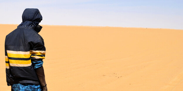Ein Man steht in der Wüste mit dem Rücken zum Betrachter.
