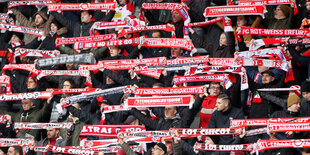 Fußballfans auf einer Tribühne halten ihre Schals hoch.