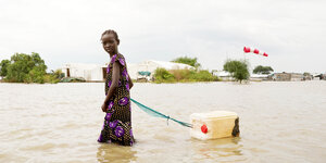 Ein Mädchen läuft durch uberflutetes Gelände und zieht einen Plastikkanister hinter sich her.
