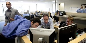 Drei Männer gucken in Redaktionsräumen auf einen Computer-Bildschirm
