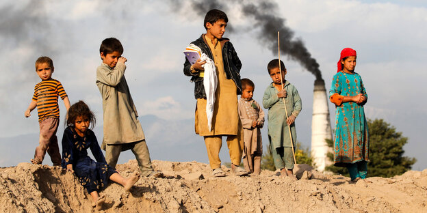 Kinder stehen auf einem Hügel vor einem rauchenden Schornstein