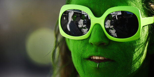 Frau mit grün geschminktem Gesicht und grüner Brille