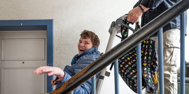 Ein lachender Junge im Rollstuhl wird die Treppe hinuntergelassen