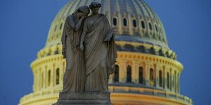 Eine Statue, die Trauer repräsentiert legt den Kopf auf die Schulter einer Statue, die Geschichte repräsentiert. Im Hintergrund die Kuppel des Capitols.
