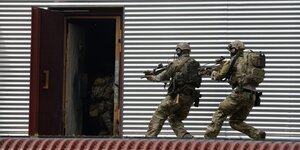 Soldaten in Flecktarn und Gewehr vor einem Gebäude