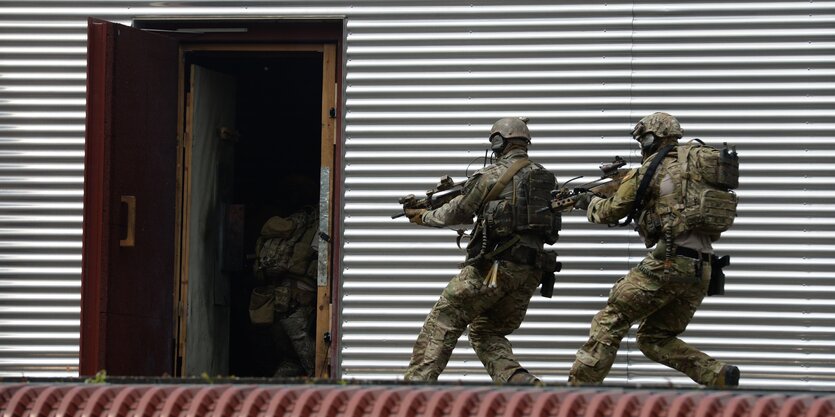 Soldaten in Flecktarn und Gewehr vor einem Gebäude