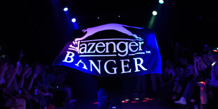 Ein Mann läuft auf einem Laufsteg und hält ein Handtuch mit der Aufschrift "Slazenger Banger" über seinen Rücken