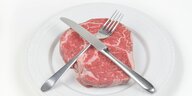 Ein Stück Fleisch liegt auf einem weisssen Teller, Messer und Gabel überkreuzt