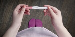 Frau mit lackierten Nägeln schaut auf einen Schwangerschaftstest
