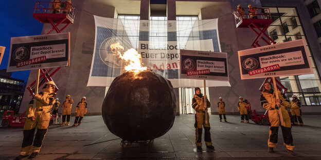 brennende Kugel plus Aktivisten mit Schildern "Stop Adani" vor Gebäude