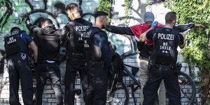 Polizisten kontrollieren 2 Mäner an einer Wand
