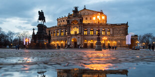 bei regnerischem Wetter spiegelt sich die erleuchtete Semperoper in einer Pfütze