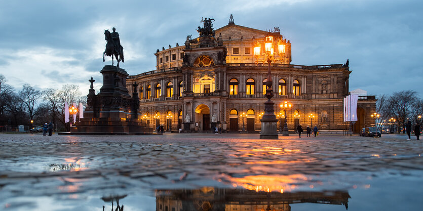 bei regnerischem Wetter spiegelt sich die erleuchtete Semperoper in einer Pfütze