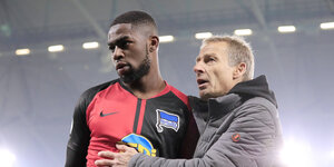 Schwarzer Fußballspieler im Hertha-Trikot, weißer Mann mit Jacke spricht mit ihm