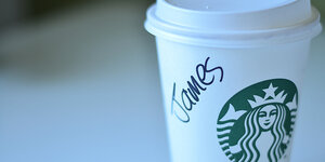 Hand greift nach Starbucks-Becher, darauf steht "James" mit Marker geschrieben (Screenshot)