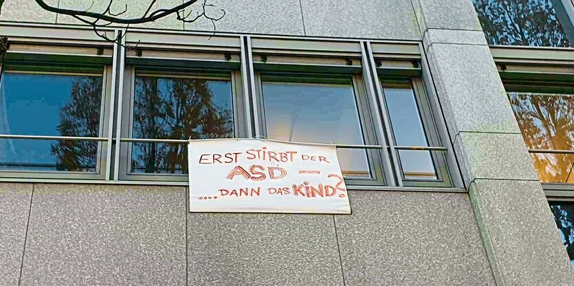 Aus einem Bürofenster hängt ein weißes Laken mit Schrift