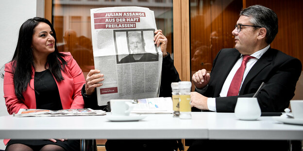 Sevim Dagdelen Günter Wallraff und Sigmar Gabriel sitzen zusammen an einem Tisch und halten ein Plakat hoch auf der Assange abgebildet ist