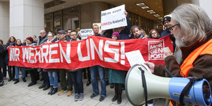 Kleine Demo, ein langes Transpi mit "Wir wehren uns", im Vordergrund ein Mikrofon