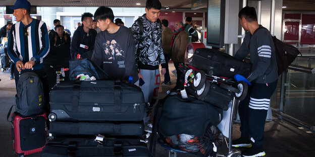 Chinesische Fußballer stehen in einer Flughafenhalle mitsamt ihrem Gepäck