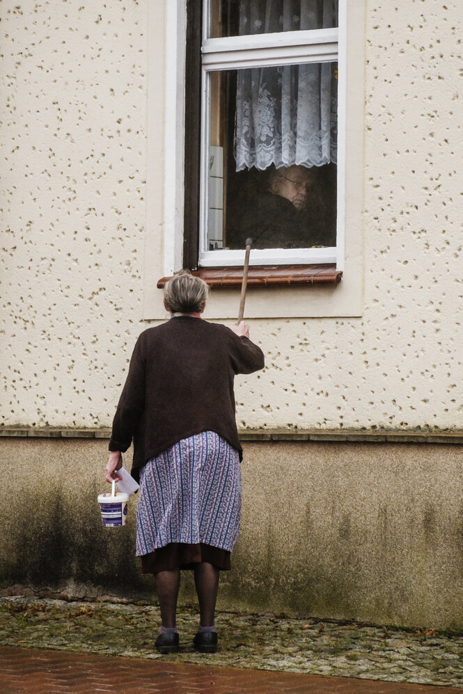 Eine ältere Dame klopft von Außen an ein Fenster