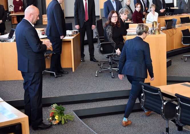 Blumenstraus liegt vor einem Mann, Frau geht weg, dahinter gucken Leute schockiert