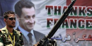 Kämpfer mit Riesenwaffe, dahinter Sarkozy-Plakat