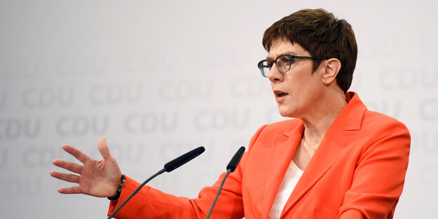 CDU-Vorsitzende Kramp-Karrenbauer steht in orangefarbenem Jacket an einem Rednerpult und spricht zu im Bild nicht auftauchenden MedienvertreterInnen