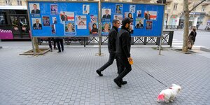 zwei Männer mit einem Hund an der Leine gehen an Wahlplakaten in Baku vorbei