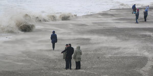 Passanten blicken auf hohe Wellen, die auf den Strand zukommen