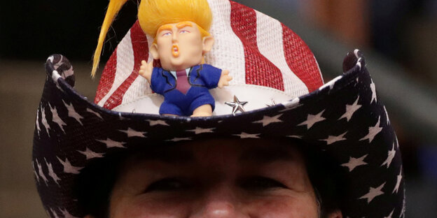 Ein Mann trägt einen Cowboyhut in den Farben der US-Flagge Darauf sitzt eine Trump-Puppe