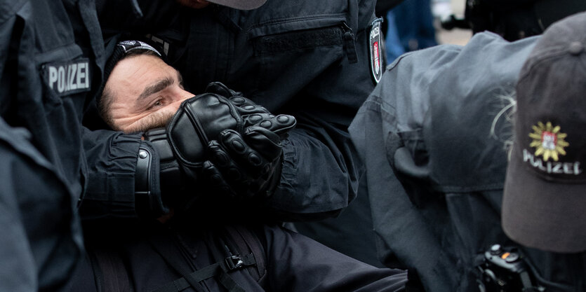 Polizisten lösen eine Sitzblockade auf und umklammern dabei den Kopf eines Teilnehmers.